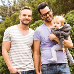 Two men holding hands while one carries a toddle